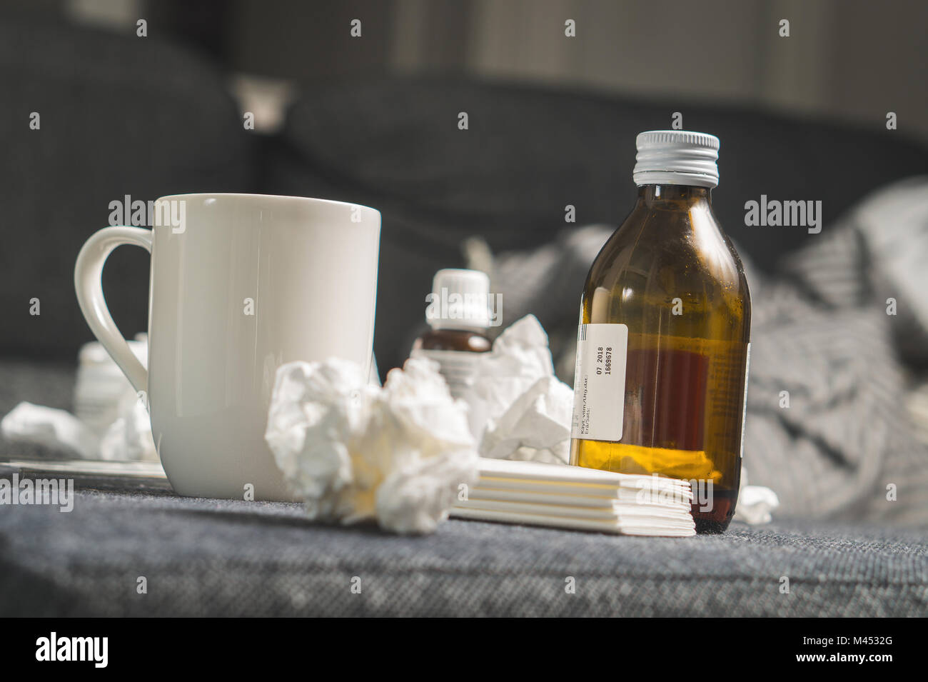Cold medicine, cough syrup, hot beverage, paper towels and tissues to beat sickness, fever or flu. Get well kit on table or sofa couch. Being ill. Stock Photo