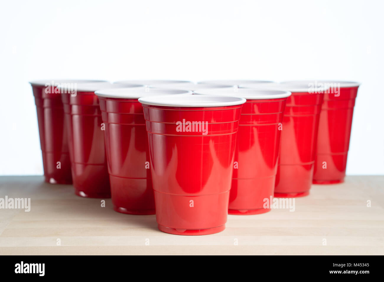Red party cups on wooden table for beer pong tournament isolated on white. College alcohol containers with free empty blank copy space for text. Stock Photo
