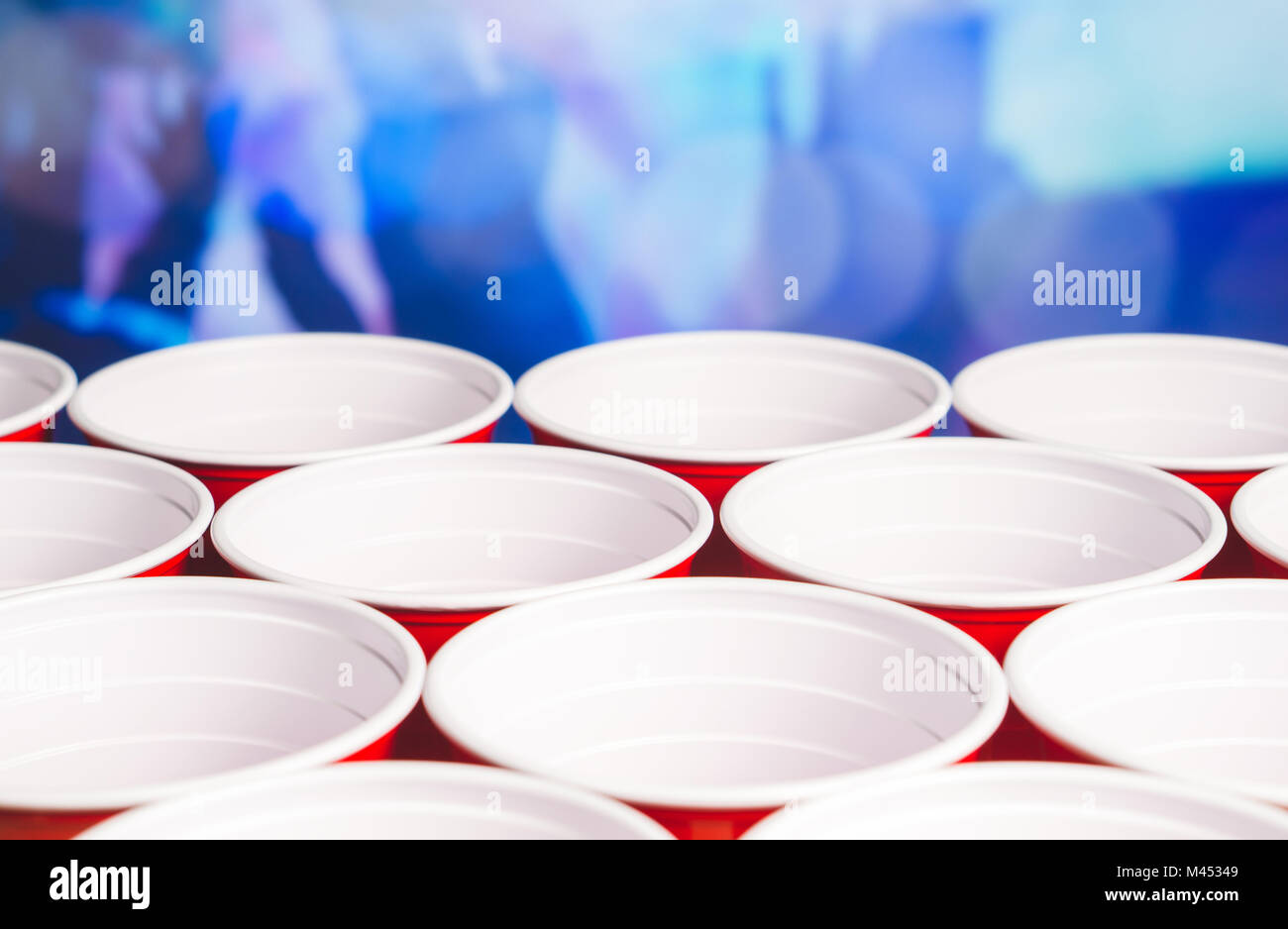 Many red party cups with blurred celebrating people in the background. Low angle close up of college alcohol containers. Marketing and promotion. Stock Photo