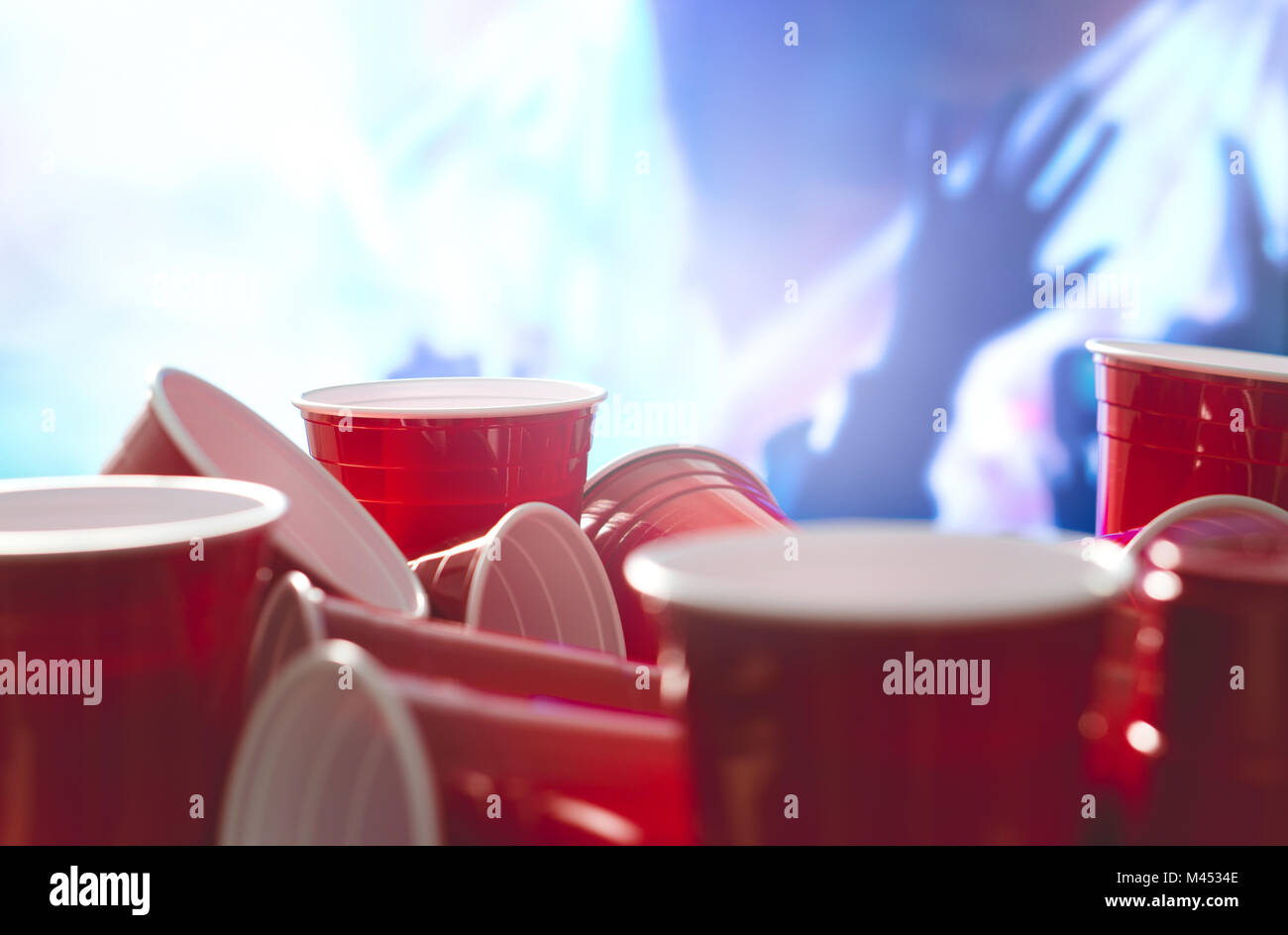Many red party cups with blurred celebrating people in the background. College alcohol containers in mixed positions. Stock Photo