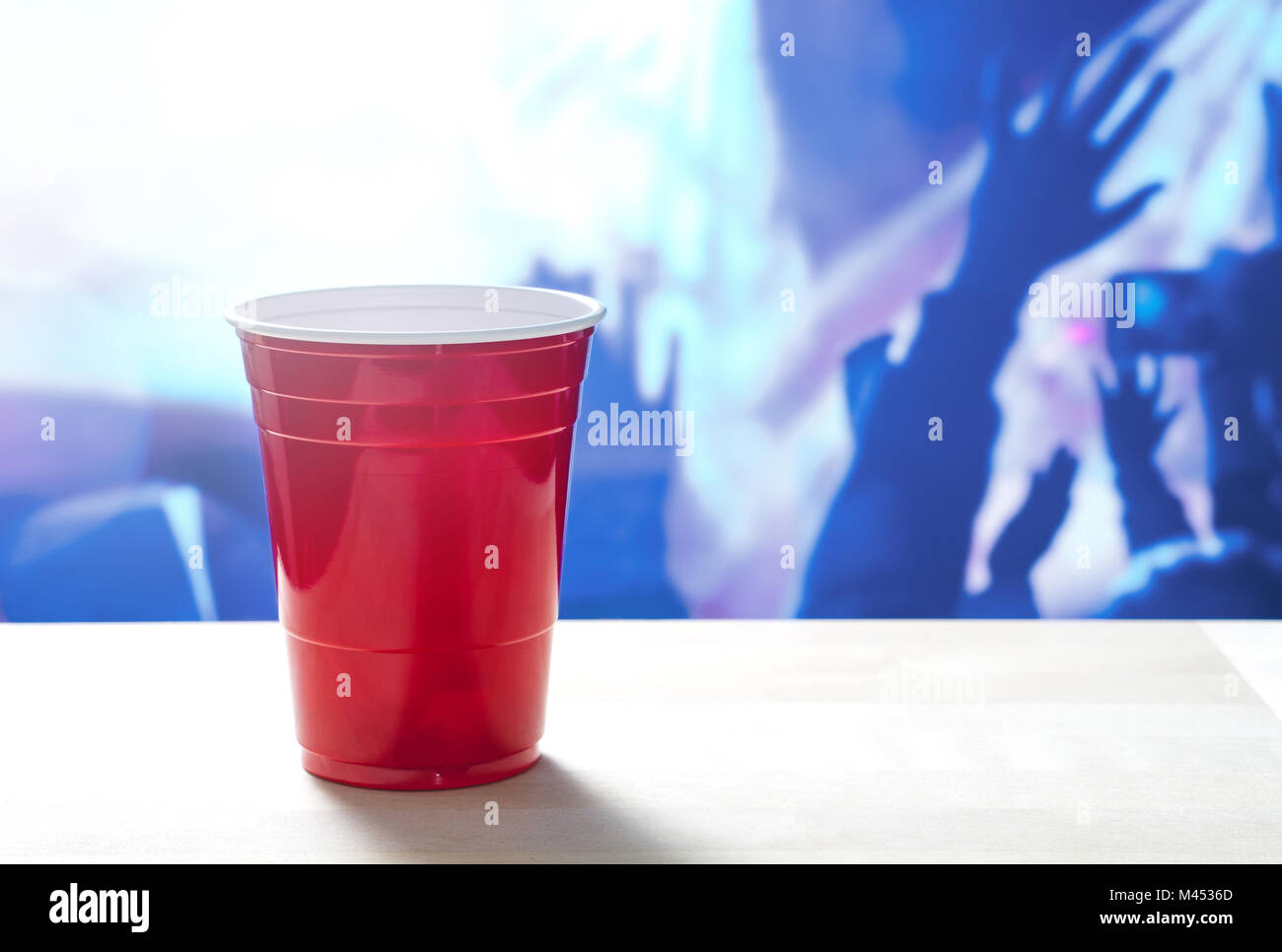 Plastic red party cup on a table. Nightclub full of people dancing on the dance floor in the background. Disco lighting. Perfect for marketing. Stock Photo