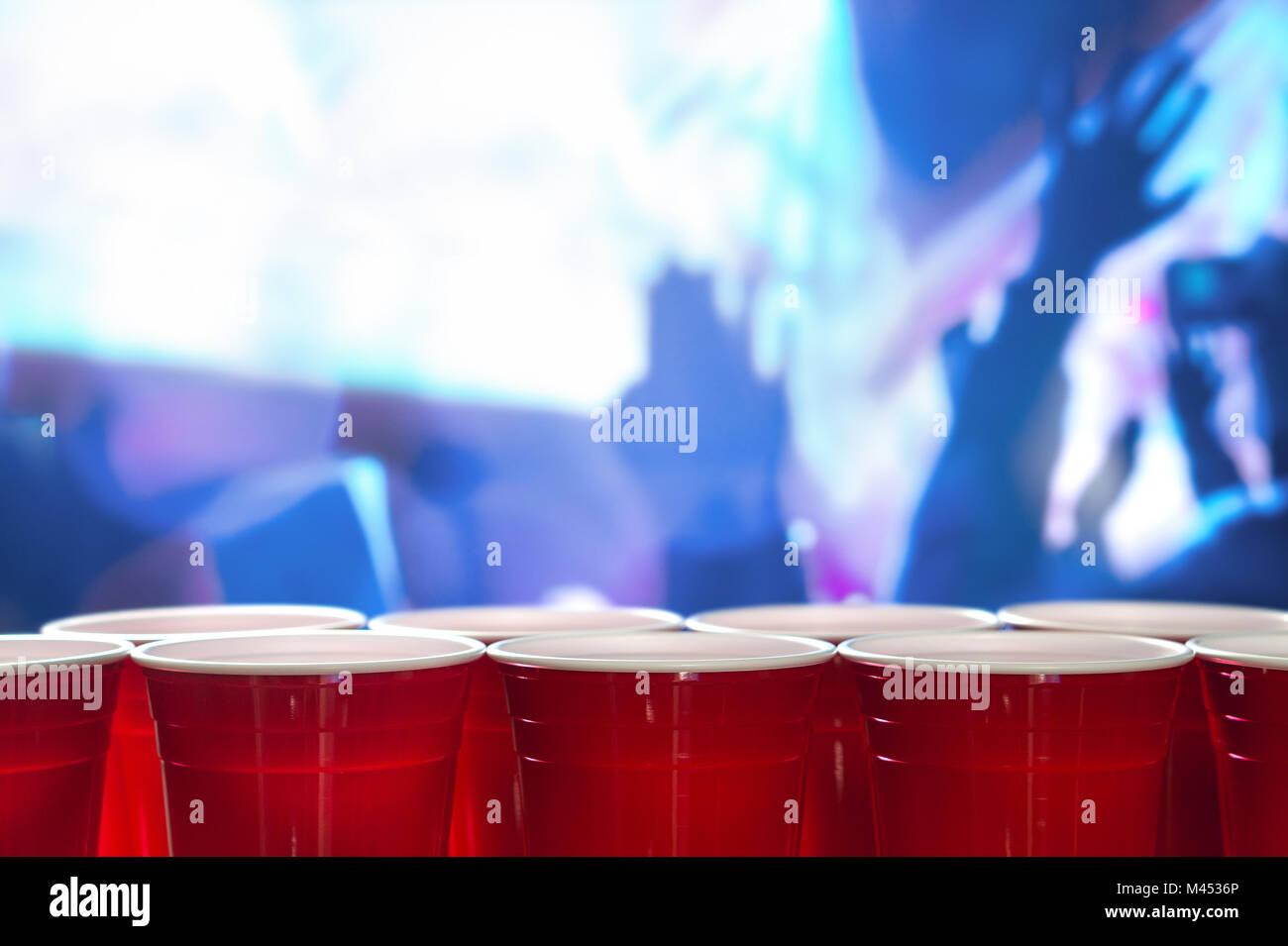Plastic red party cups in a row in a nightclub full of people dancing on the dance floor in the background. Perfect for marketing and promotion. Stock Photo