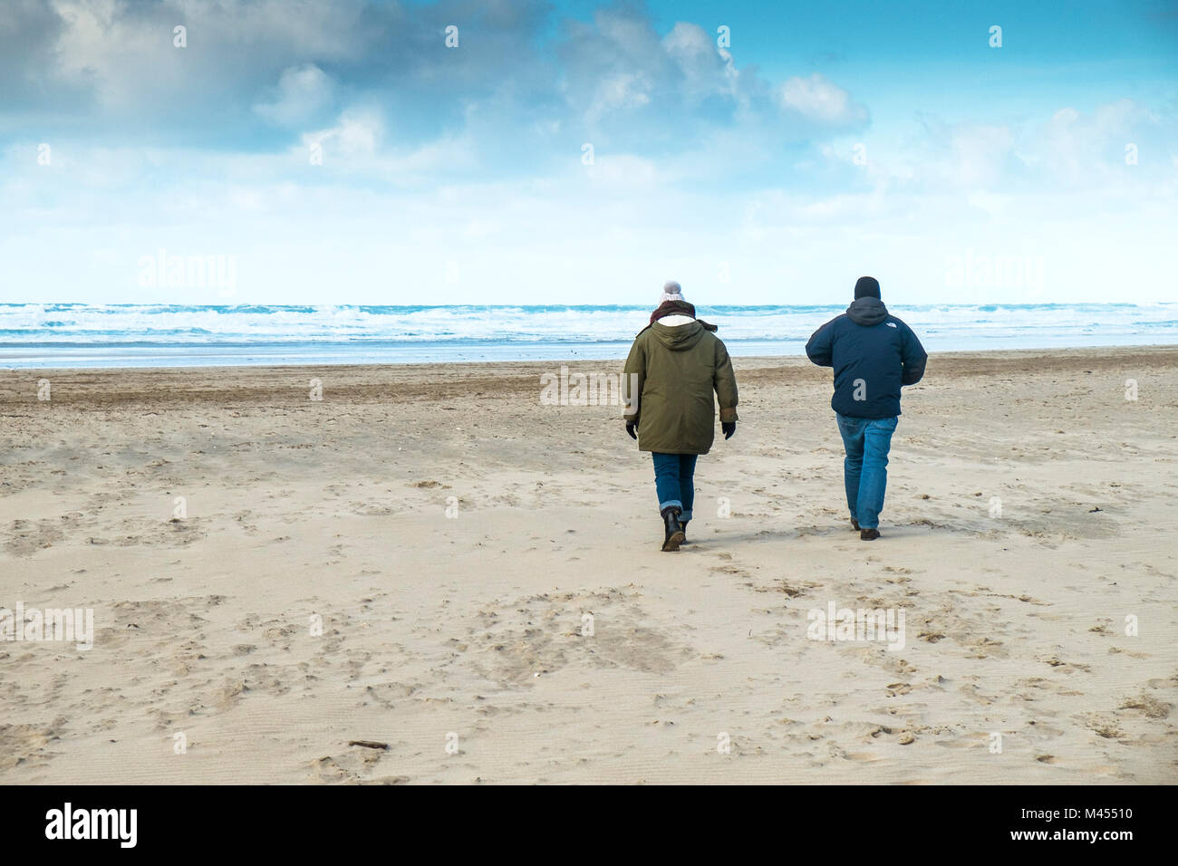 Two people wrapped up against the cold weather walking on a beach. Stock Photo