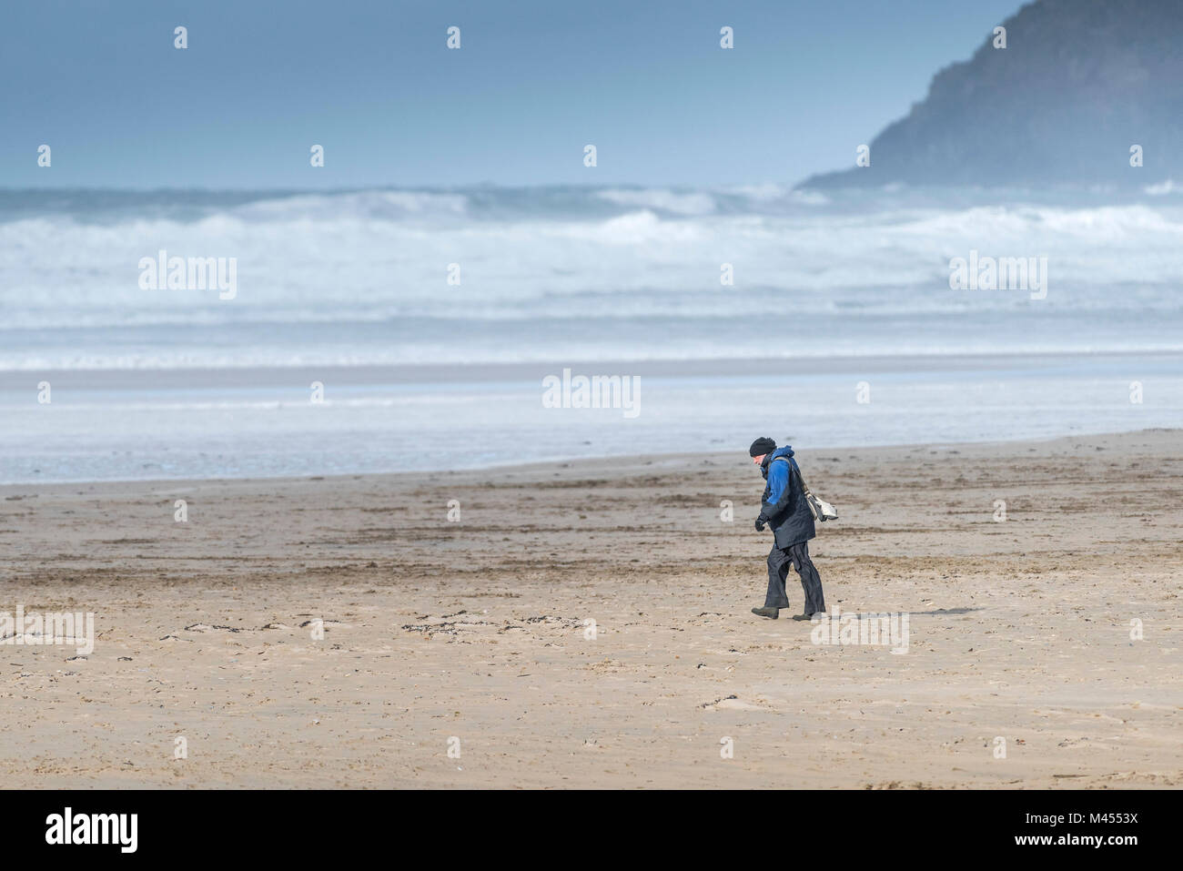A lone man walking into the wind on Perranporth Beach in Cornwall UK. Stock Photo