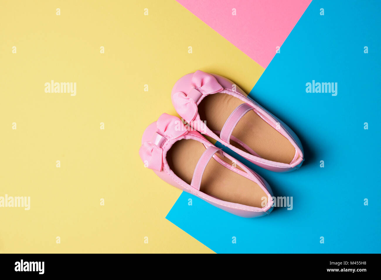 high angle view of a pair of pink patent leather shoes on a yellow, blue and pink background, with some blank space Stock Photo