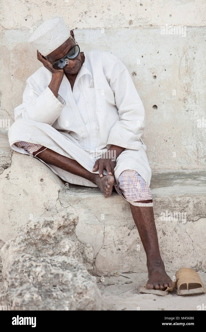 Stone Town, Zanzibar Island,Tanzania, 05/28/2015.  Old Man asleep sitting against wall in Stone Town, Zanzibar Island, Tanzania. Stock Photo