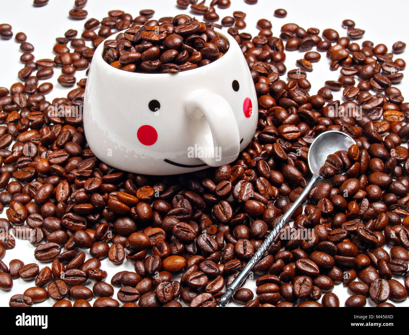 A white coffee mug filled with grains of roasted coffee stands on a pile of coffee beans Stock Photo