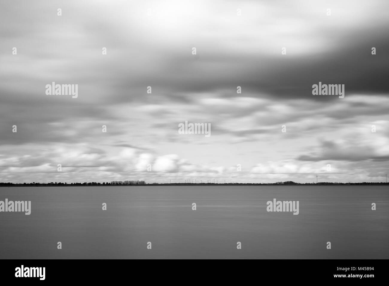 Long exposure shot over a lake with moving clouds in black and white. Stock Photo