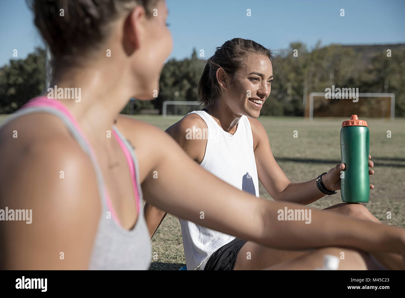 Women sitting on football pitch drinking from water bottle Stock Photo