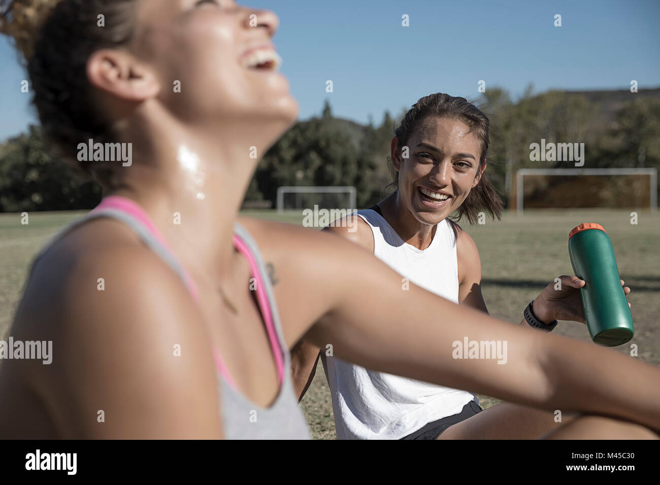 Women sitting on football pitch drinking from water bottle Stock Photo
