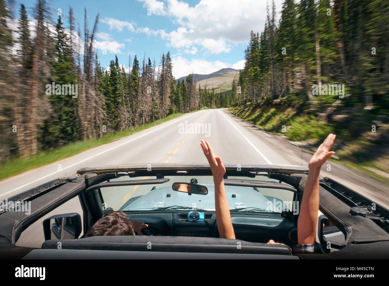 Road trip couple driving convertible on rural highway with hands raised, Breckenridge, Colorado, USA Stock Photo
