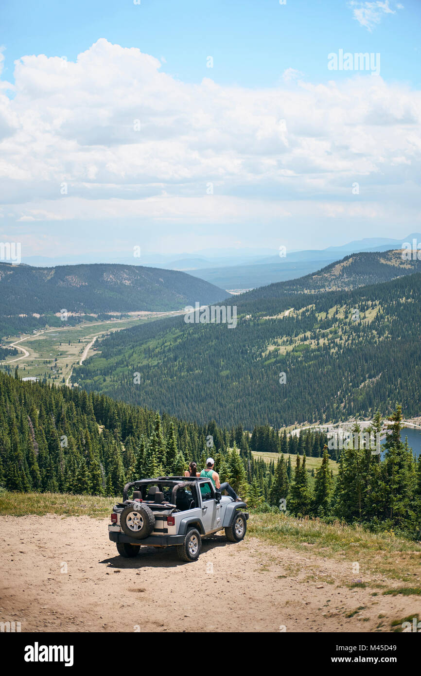 Road trip couple looking out at mountains from off road vehicle hood, Breckenridge, Colorado, USA Stock Photo
