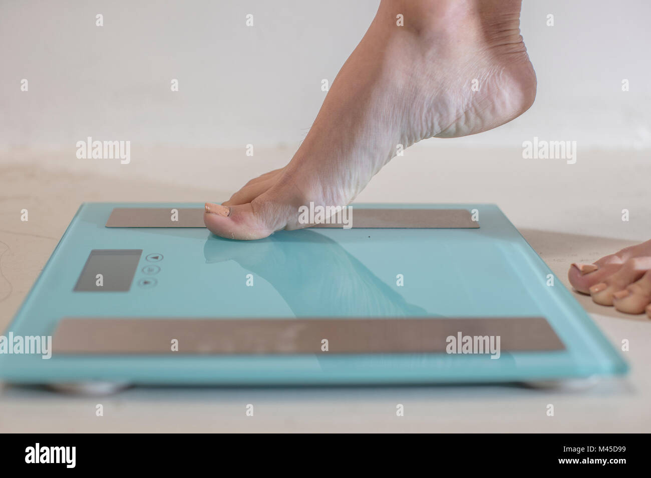 Young woman stepping onto weighing scales, close up of foot Stock Photo