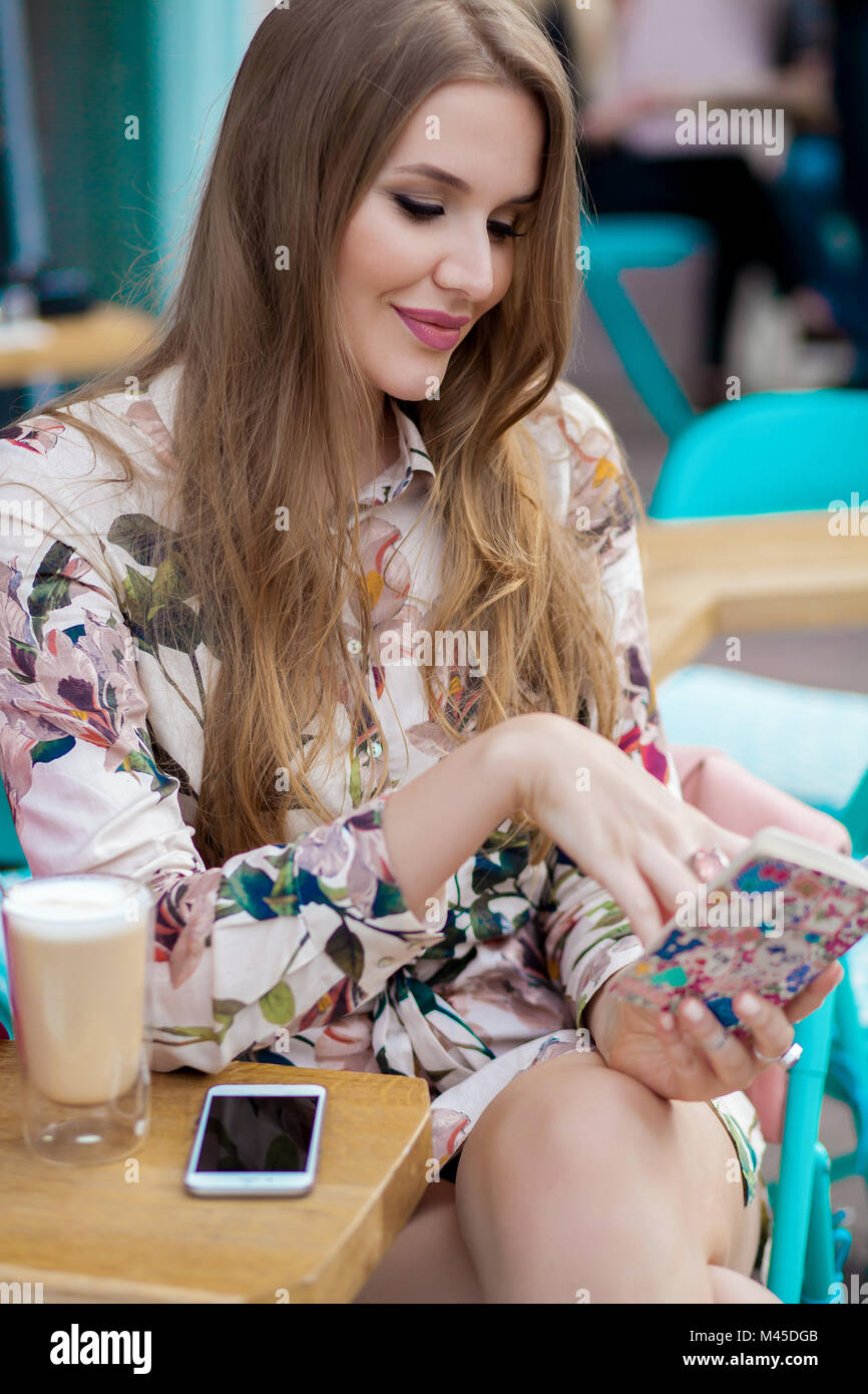 Stylish young woman with long hair reading notebook at sidewalk cafe, Odessa, Ukraine Stock Photo