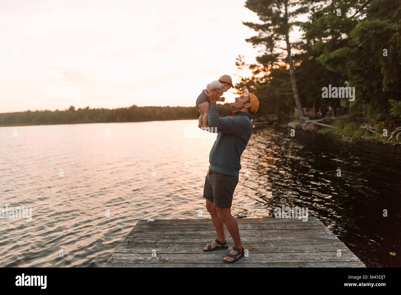 Man holding up baby daughter on lake pier Stock Photo