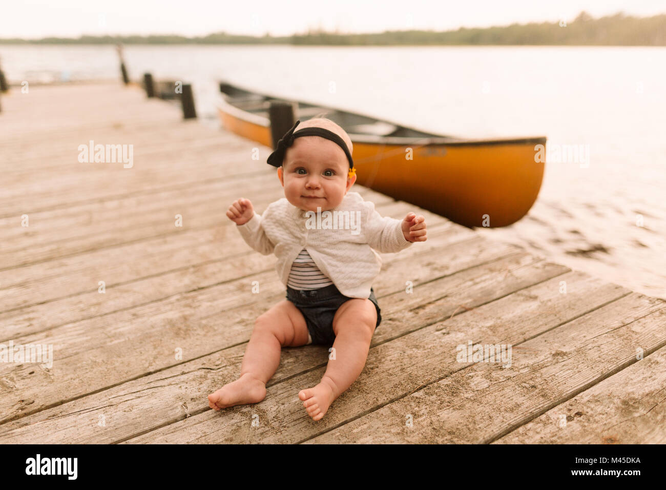 Portrait of baby girl sitting on lake pier Stock Photo