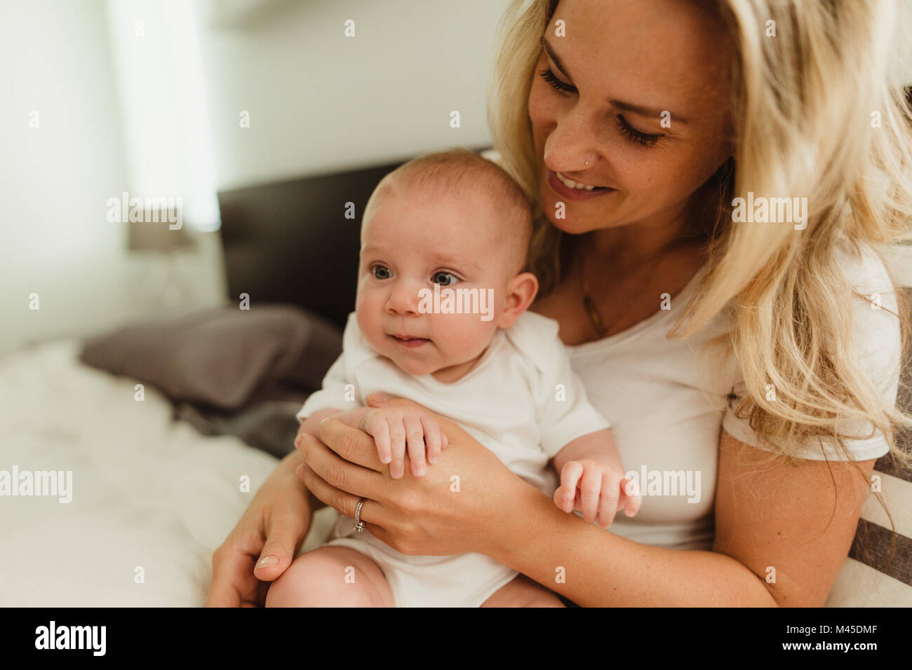Baby girl sitting on mother's lap on bed Stock Photo