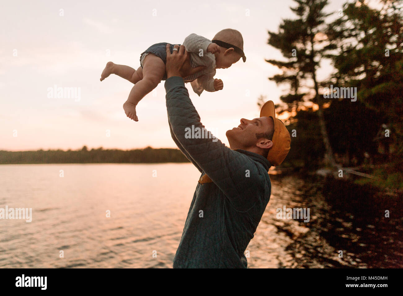 Man holding up baby daughter at lakeside Stock Photo