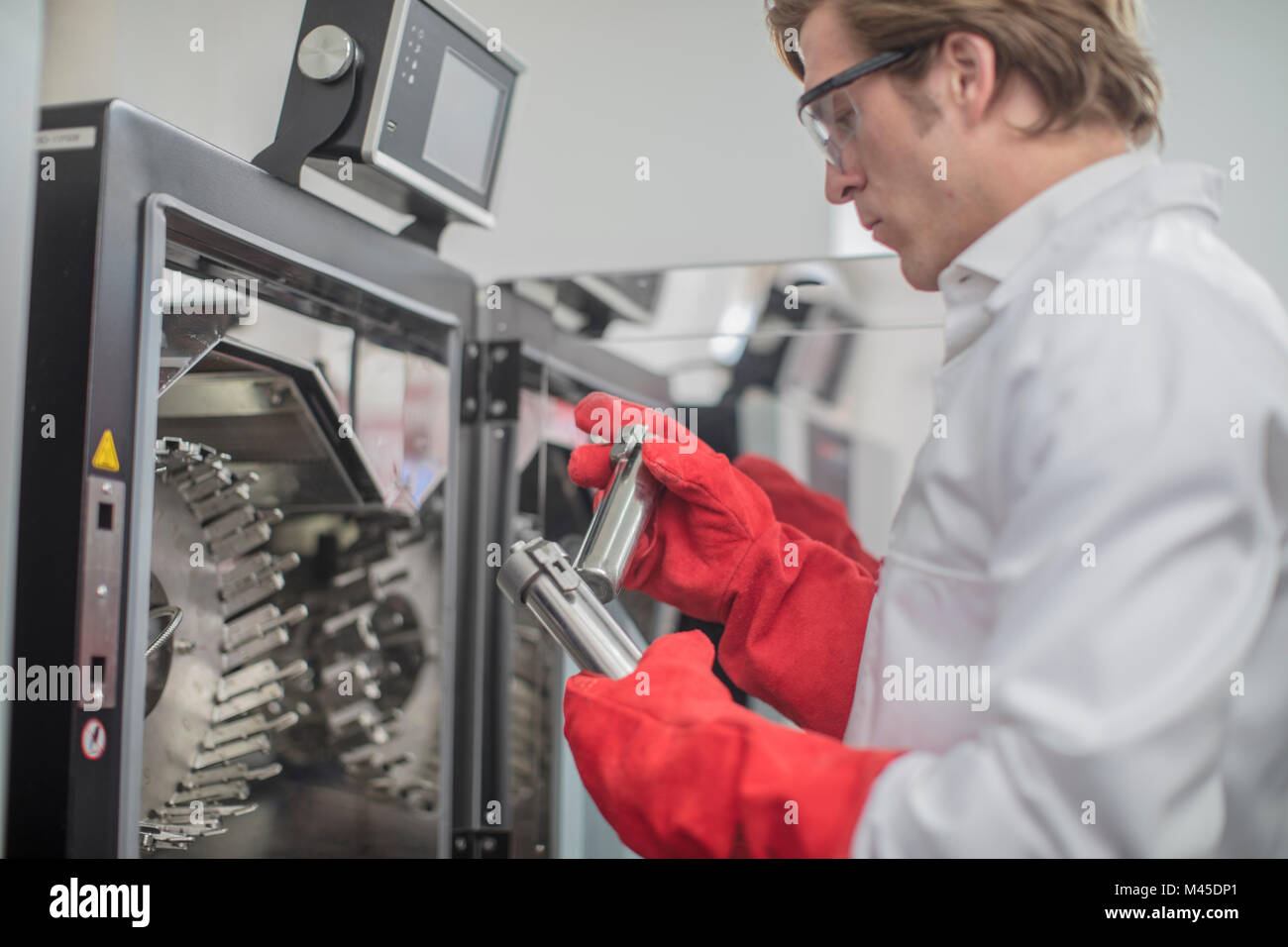 Male worker in thread factory, taking beakers from chemical oven Stock Photo