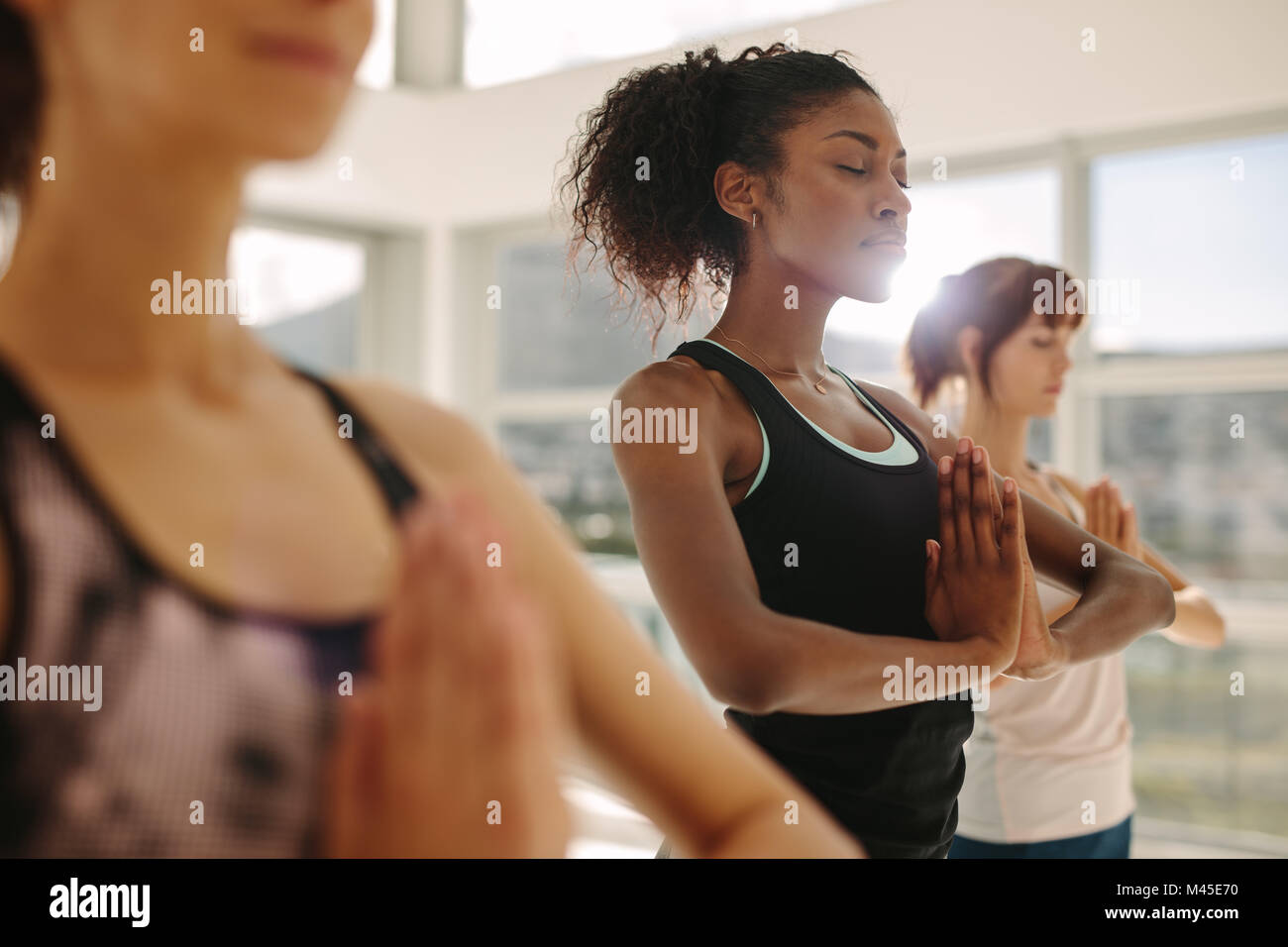 Fit young woman practice yoga with friends. Fitness female doing yoga meditation indoors in gym class. Stock Photo