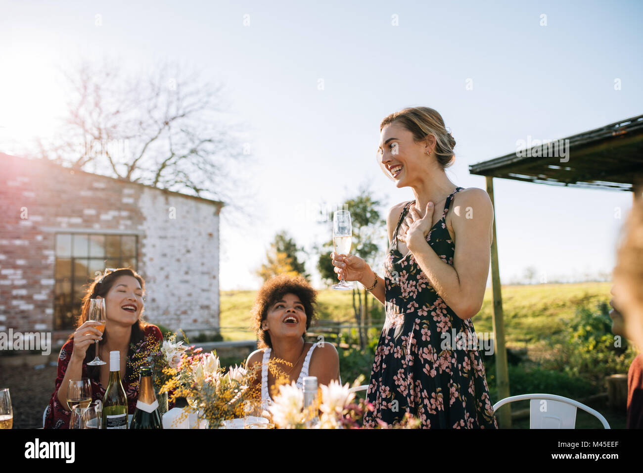 Overwhelmed woman sharing good news with friends at garden restaurant. Friends celebrating a special occasion at outdoor summer party. Stock Photo
