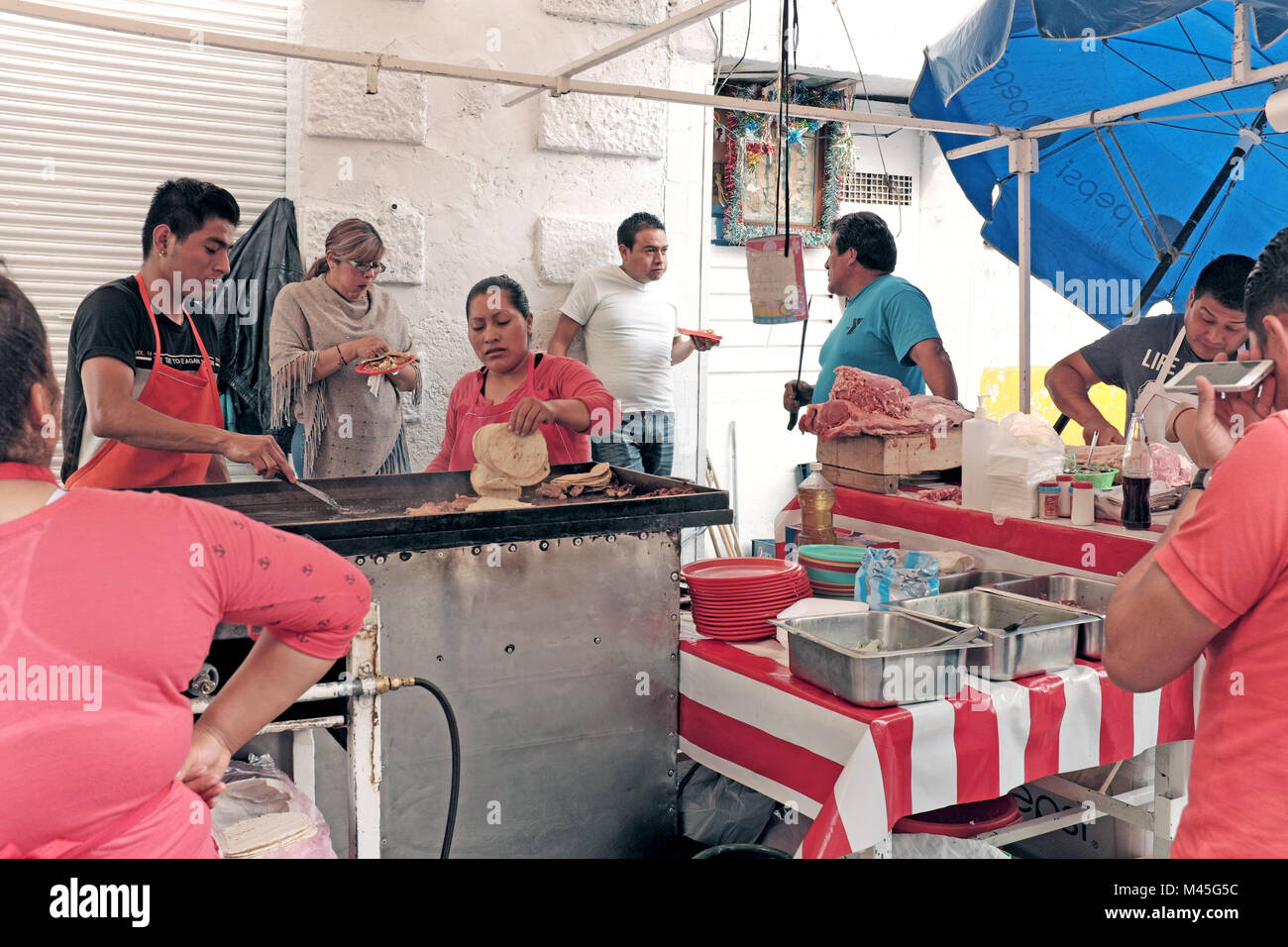 A street food stand in Mexico City, Mexico shows unsanitary conditions with raw meat and food sitting out and workers not using gloves while cooking Stock Photo