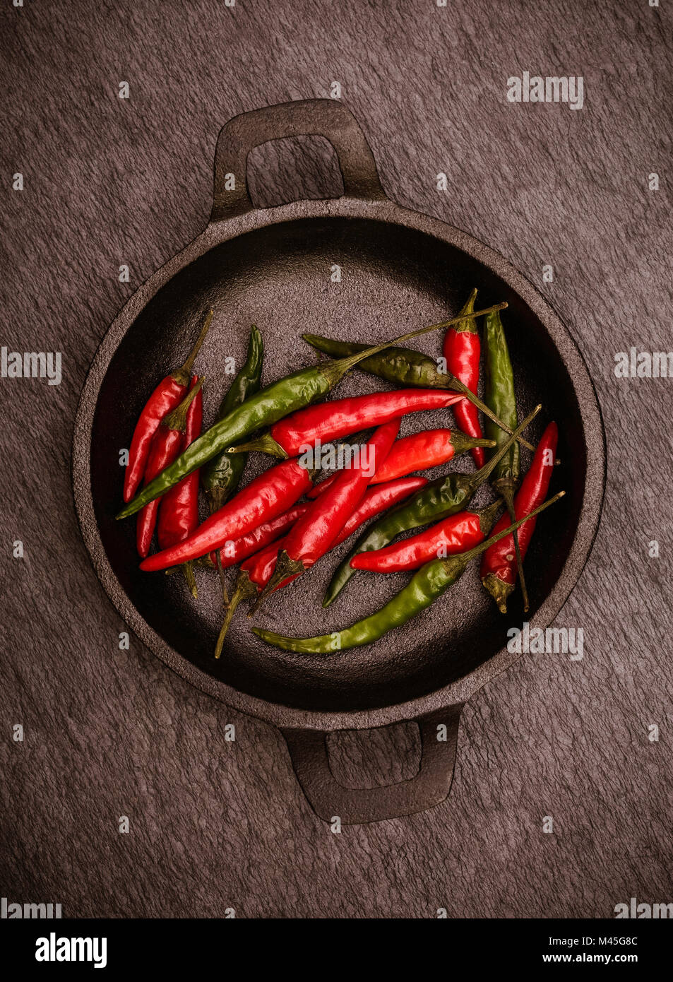Red and Green Chillies in a black cast Iron bowl on a black rustic slate background Stock Photo