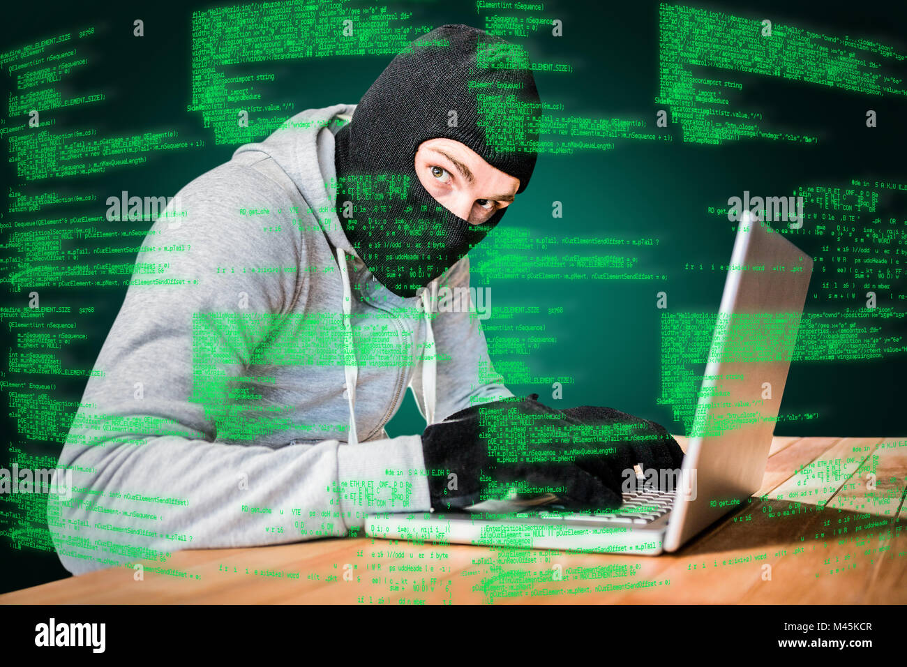 Composite image of focused thief with hood typing on laptop Stock Photo