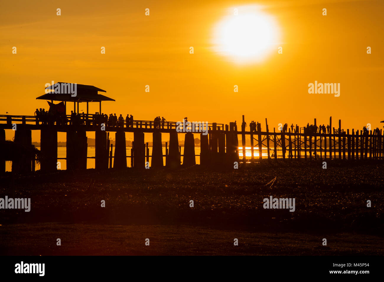 Sunset over the lake near wooden foot bridge U Bein Bridge crossing the ...