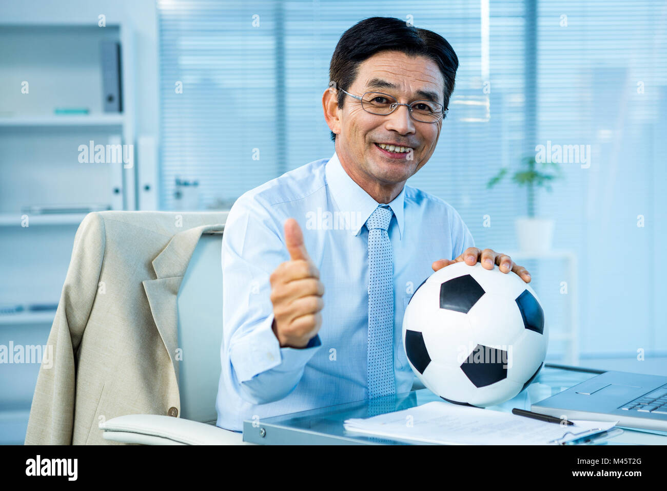 Asian businessman holding soccer ball with thumps up Stock Photo - Alamy
