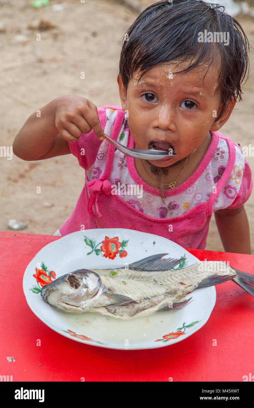 Child eating and cooking fish in Bagan Myanmar Stock Photo