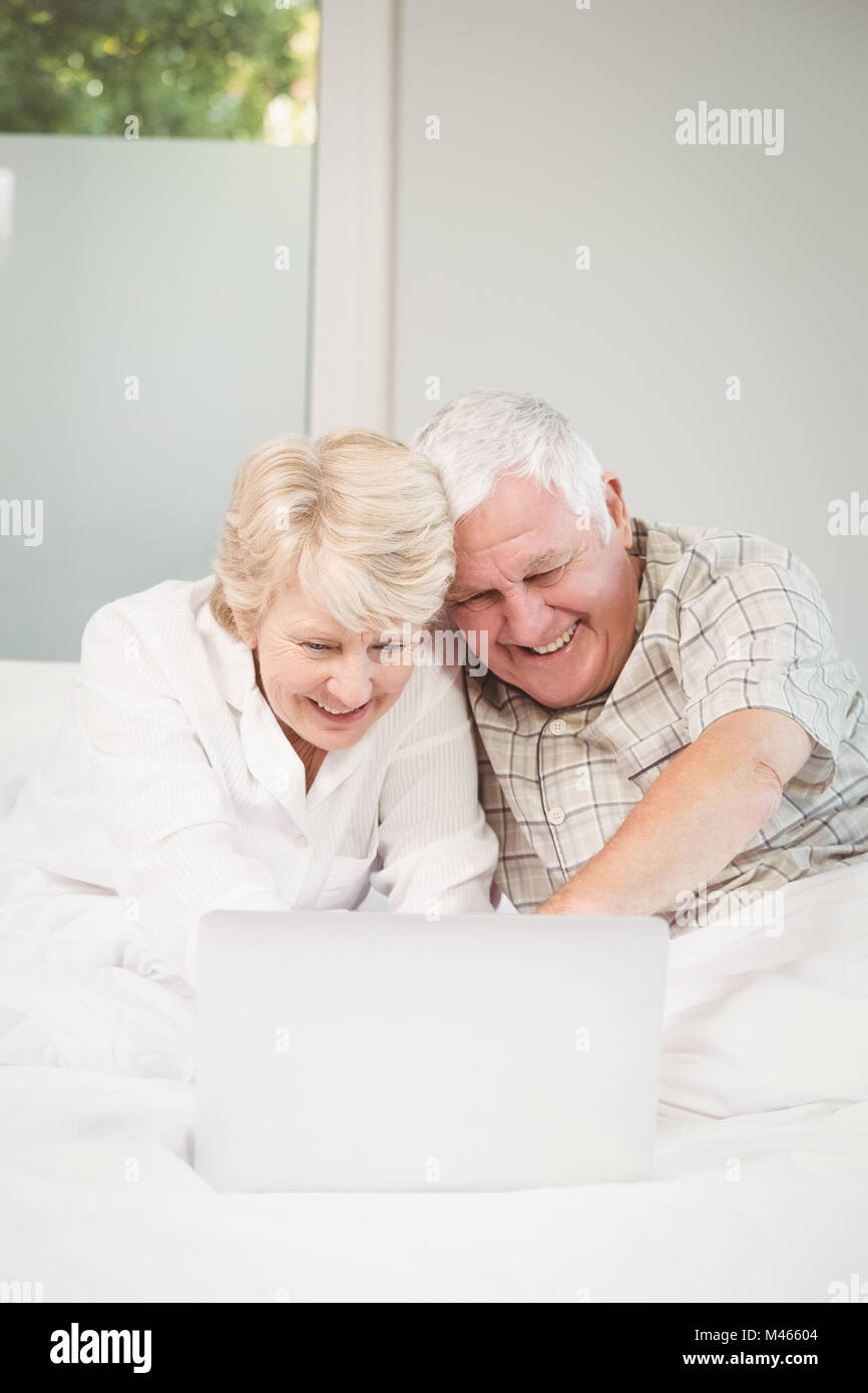 Happy couple laughing while using laptop in bed Stock Photo - Alamy