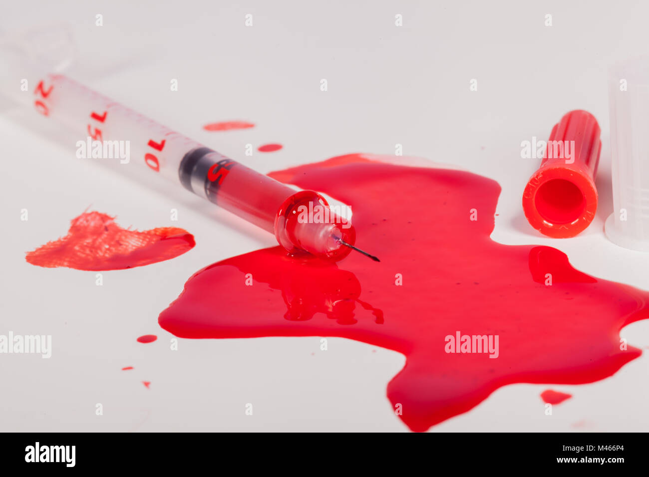 Syringe Squirting Red Blood onto White Background Stock Photo