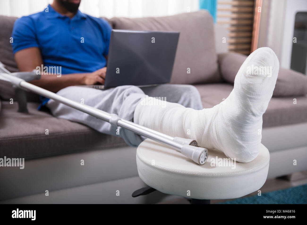Man With Broken Leg Sitting On Sofa Using Laptop Stock Photo
