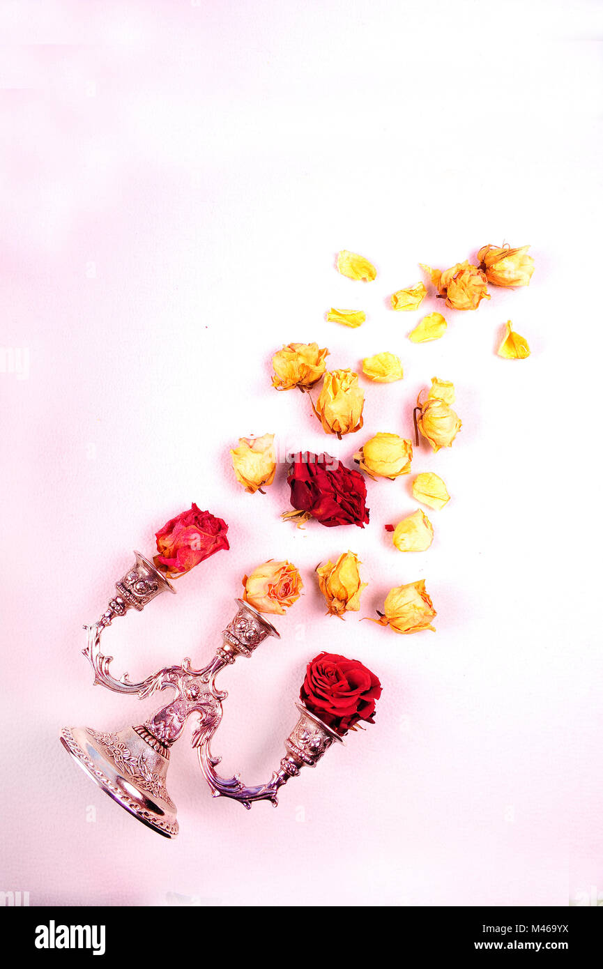 Vertical shot of three armed silver candelabra. Faded roses and rose petals flying out of the candle holder.  Flat lay arrangement on white background Stock Photo