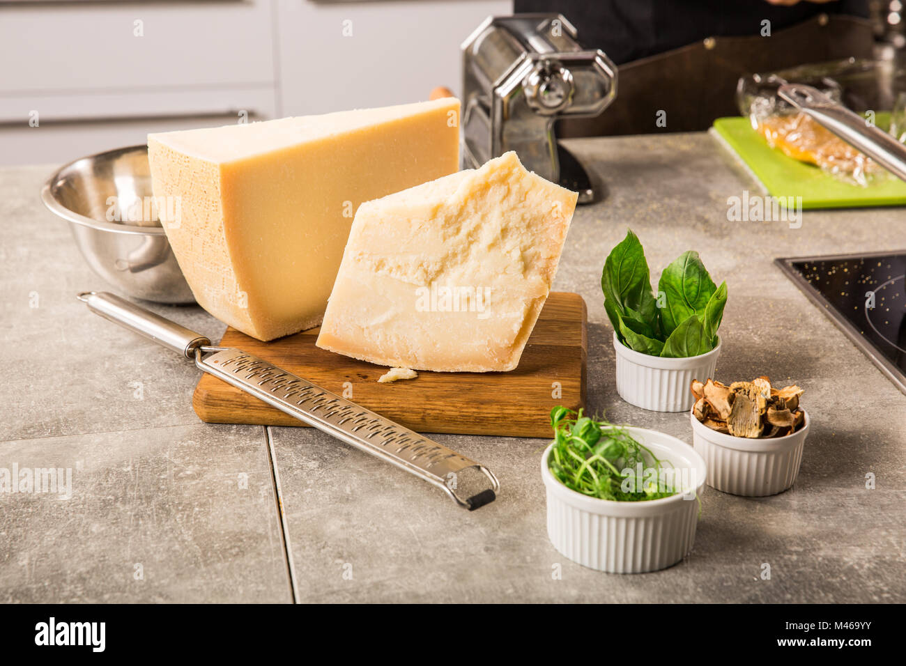 grated parmesan cheese and metal grater on wooden board with greenery in the kitchen Stock Photo