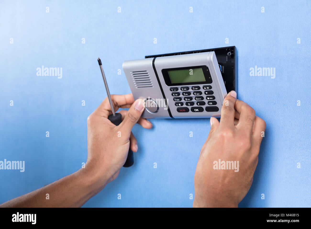 Human Hand Installing Security System On Blue Wall Stock Photo