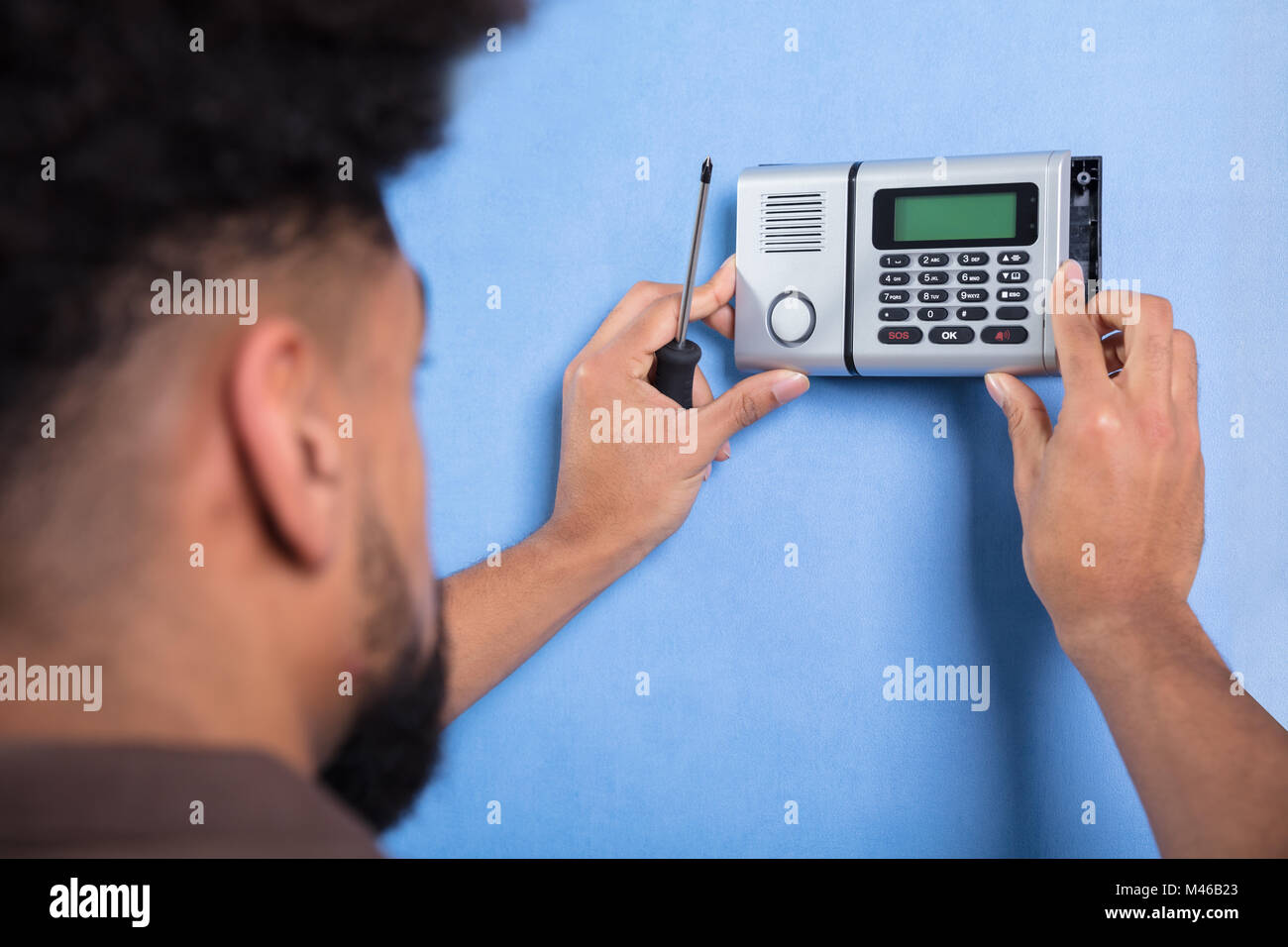 Close-up Of A Man Installing Security System On Blue Wall Stock Photo