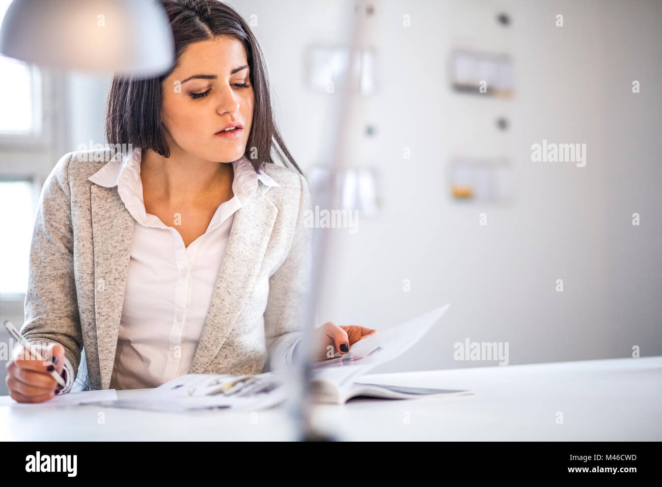 Businesswoman reading brochure while taking notes in office Stock Photo
