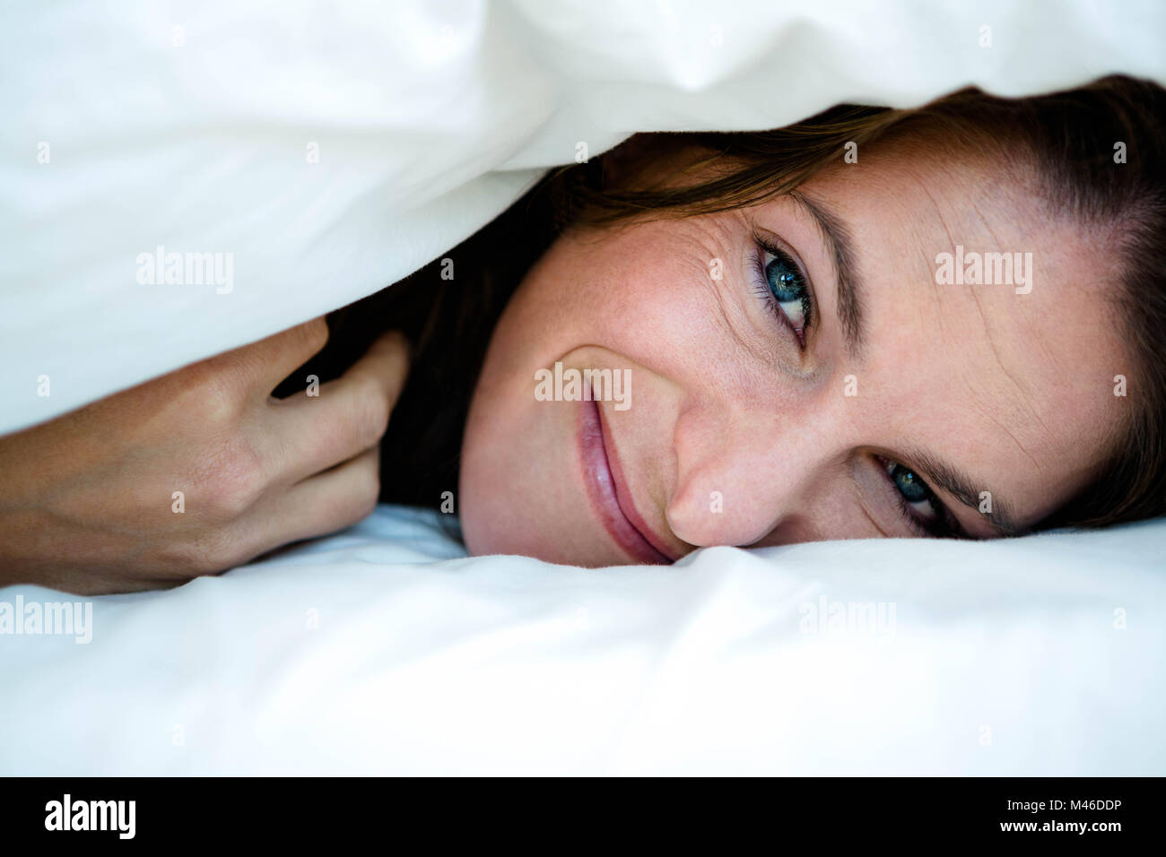 smiling woman peering  out from under a duvet Stock Photo