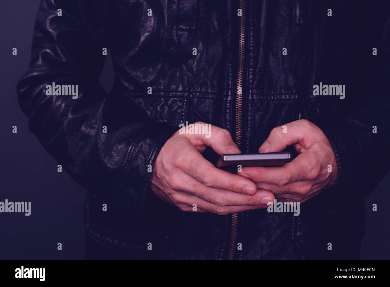 Man in leather jacket using mobile phone for texting. Modern technology and lifestyle concept, ultra violet toned shadows Stock Photo