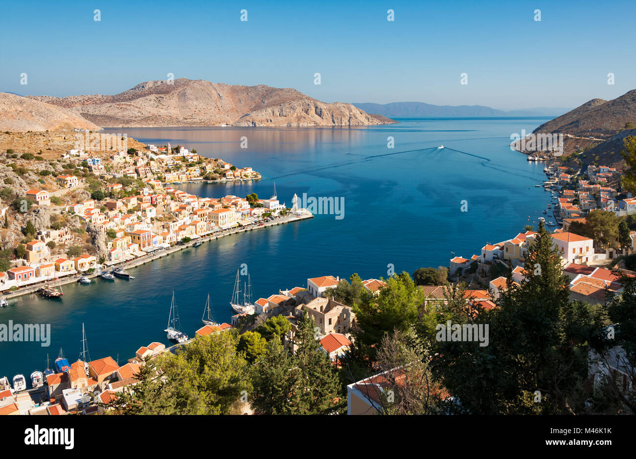 Panorama view of the village and port Gialos on the Greek island of Symi and the uninhabited islet Nimos, Dodecanese Greece, and Turkey in background Stock Photo