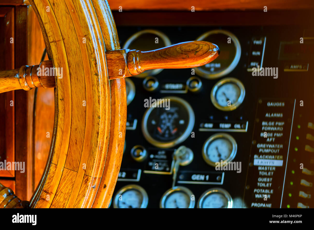 Yellow, old, lacquered, wooden steering wheel on a marine yacht, control devices, sensors, buttons and direction arrows on a black flap, in the backgr Stock Photo