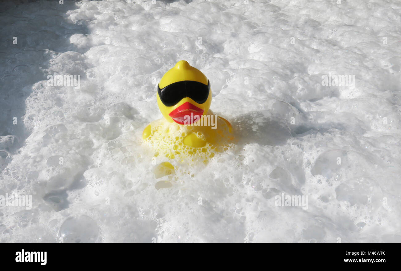 A yellow rubber duck wearing sunglasses caught in the foamy waters of a hot tub Stock Photo