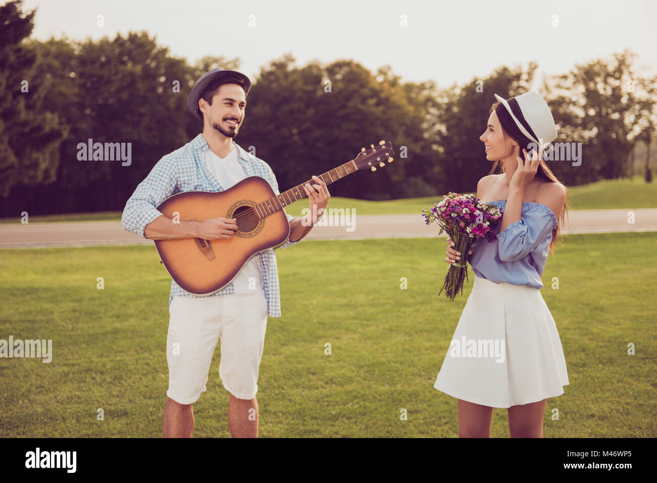 Cute sweet partners on a date outside, well dressed, excited, lovely. Good day, happiness, friendship concept. Lady holds present, guitarist plays ins Stock Photo