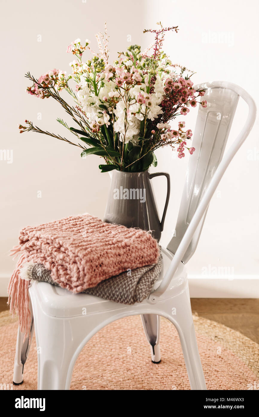 Pretty flowers in a jug styled with pink and grey scarves on a chair Stock Photo