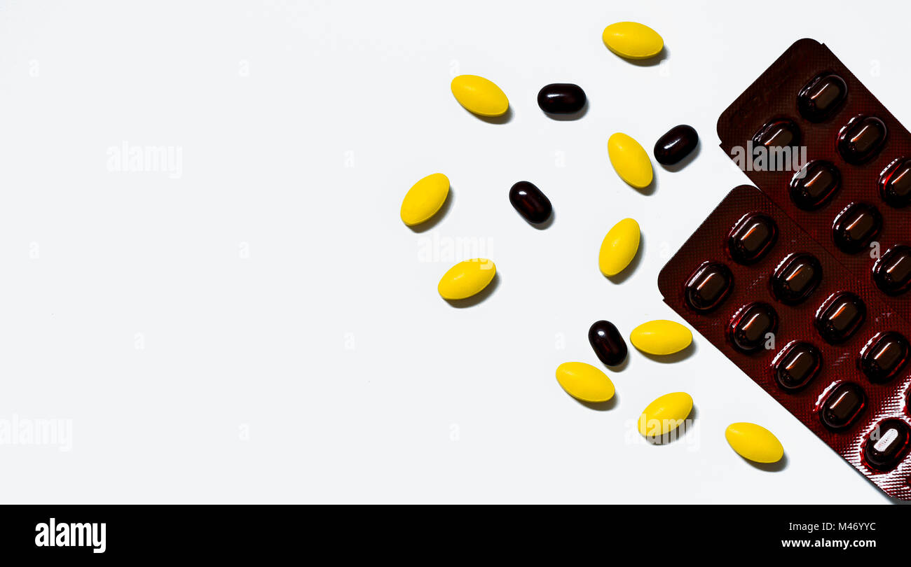 Macro shot of yellow oval tablet pills, black tablets pills on white background with creative pattern and black caplets pills in brown blister pack. P Stock Photo