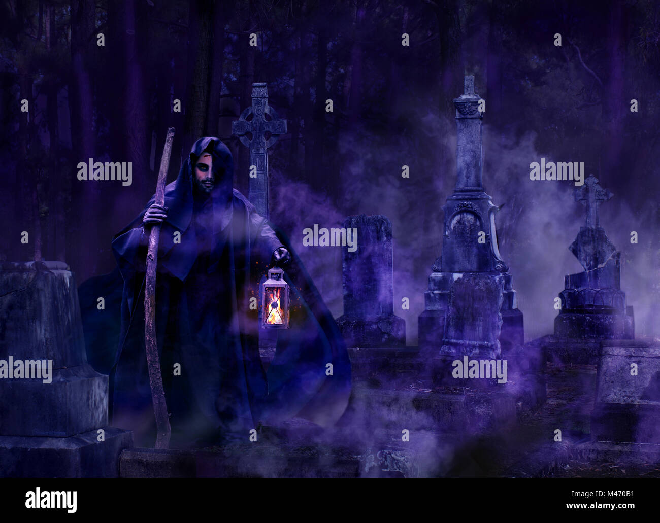 Wicked gothic man in a hooded balk robe holding a lantern walking through a foggy graveyard at night Stock Photo