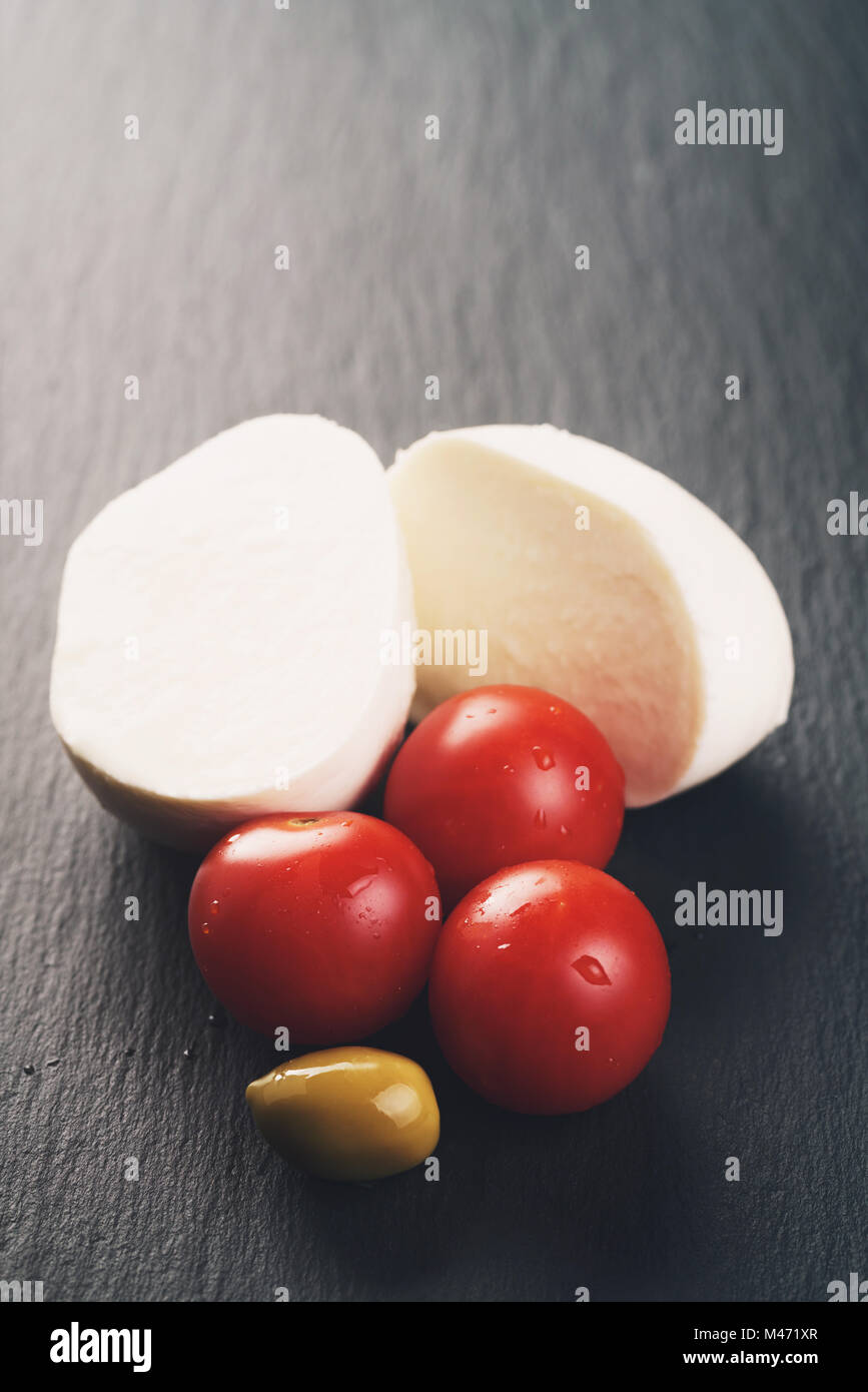 sliced mozarella ball with tomato and olives on slate background Stock Photo
