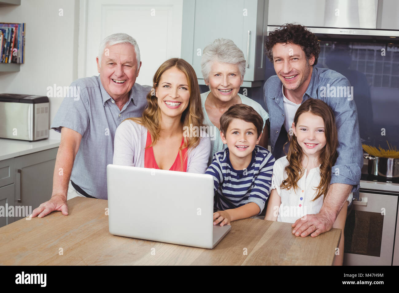 Portrait of happy family using laptop in kitchen Stock Photo - Alamy
